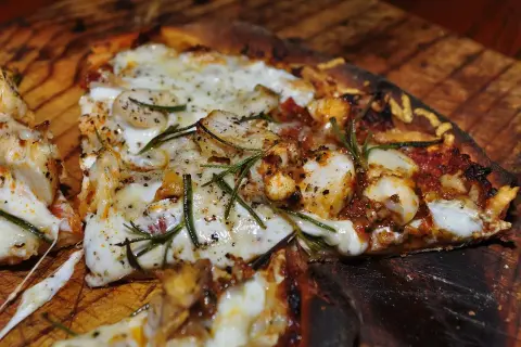 En närbild av en utsökt pizza med kyckling, ost och rosmarin. En smak av pizzans ursprung.