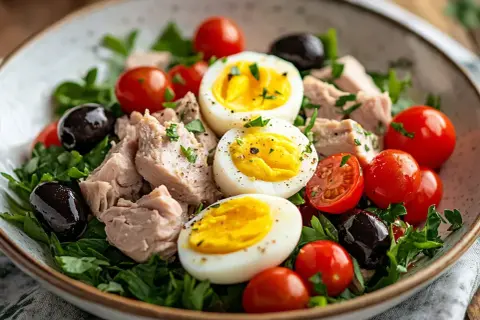 En härlig sallad nicoise med tonfisk, ägg, tomater och oliver på en bädd av gröna blad.