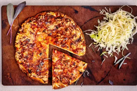 En hel och en skivad pizza på en träskärbräda, med en hög strimlad kål. En klassisk kombination som ger en hint om pizzasallad ursprung.
