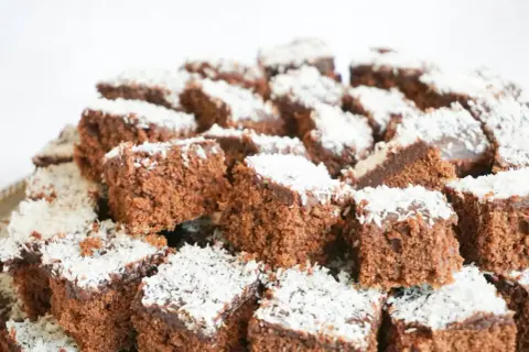 En hög med små, fyrkantiga chokladbitar, en klassisk snoddas kaka, toppade med kokosflingor.