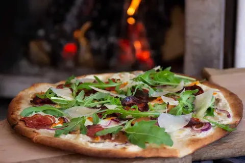 Pizza bianco med salami, ruccola och parmesan. En läcker pizza som precis kommit ut ur ugnen.