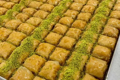 En stor bricka med gyllene, saftiga baklava-bitar, strödda med gröna pistagenötter. Perfekt för ett baklava recept.
