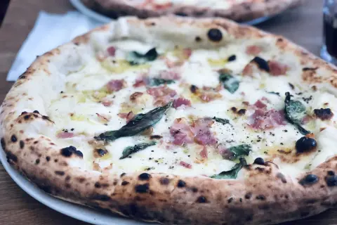 En ljuvlig pizza med bubblig lilla napoli deg, toppad med ost, bacon och basilika. Perfekt för en mysig kväll.