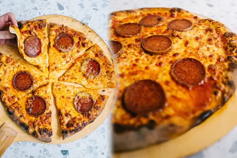 En hand tar en bit av en utsökt pepperoni pizza, perfekt för ett äkta new york pizza recept.