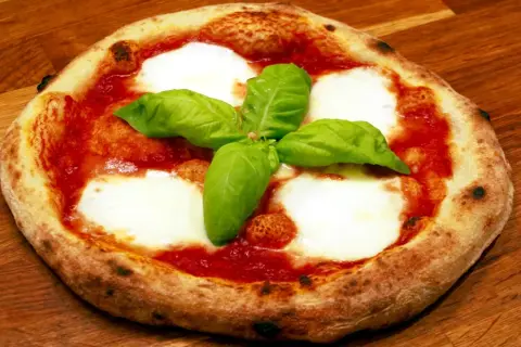 En napolitansk pizzadeg snabb, toppad med tomatsås, mozzarella och färsk basilika, ligger på en träyta.