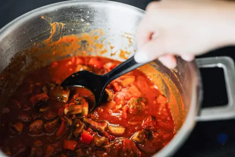 En hand rör i en gryta med mustig coq au vin, fylld med kyckling, svamp och grönsaker i en rik sås.