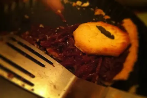 En bit paj med mörkt fyllning och gyllene lock, redo att serveras till middag trettondagsafton.