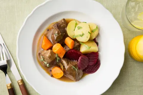 En tallrik med skånsk kalops, kött, morötter, potatis och rödbetor. Serveras med en drink med citron och is.