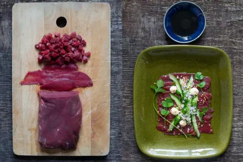 Förberedelser för asiatisk råbiff: rått kött i bitar och skivor på en skärbräda, färdig rätt med gurka, örter och sesamfrön på en grön tallrik.