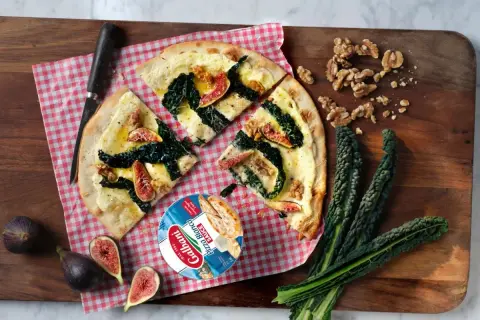 En läcker pizza sverige med fikon, grönkål och valnötter. Serveras på en träskärbräda med färska ingredienser.