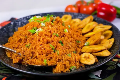 En stor portion jollof rice med stekt plantain, garnerad med salladslök. En härlig måltid!