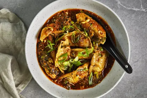 En skål med ångande dumplings i en kryddig sås, toppad med salladslök och sesamfrön. Perfekt för snabba vegetariska recept.