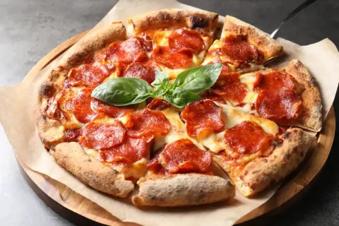 En napolitansk pizza med generöst med pepperoni som topping, toppad med färsk basilika.