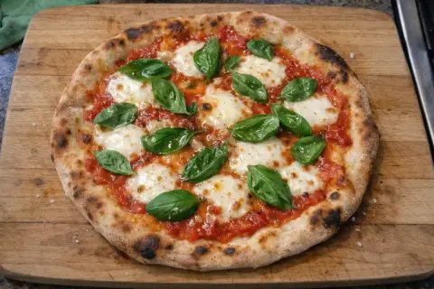 En nybakad pizza med tomatsås, smält mozzarella och färsk basilika på en träskärbräda.