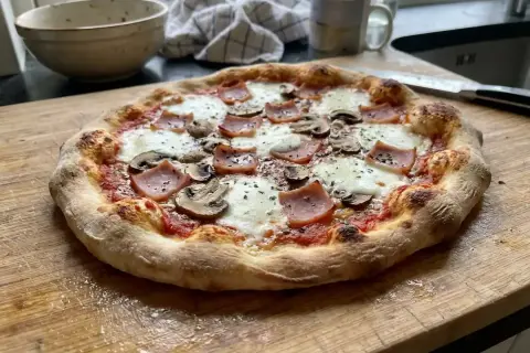 En nybakad pizza siciliana med skinka och champinjoner på en skärbräda.