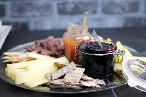 Ostbricka med kex, kött, päron och två sorters marmelad till ost. En burk med mörk bärsylt och en med ljus fruktmarmelad.