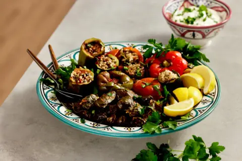 En tallrik med fyllda grönsaker och vinblad, perfekt för ett dolma recept. Serveras med citronklyftor och en skål med yoghurt.