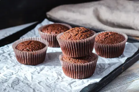 Fem choklad cupcakes på ett bakplåtspapper. Två staplade på varandra i förgrunden, med tre till utspridda runt dem.