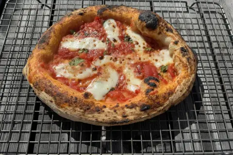 En nybakad pizza med bubblig pizzadeg 6 timmar, tomatsås och mozzarella vilar på ett galler.