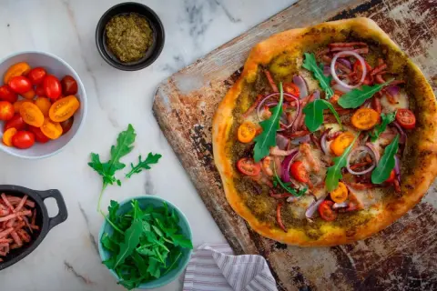 En läcker pizza bianco med parmaskinka, ruccola, körsbärstomater och rödlök. Perfekt för en mysig kväll!