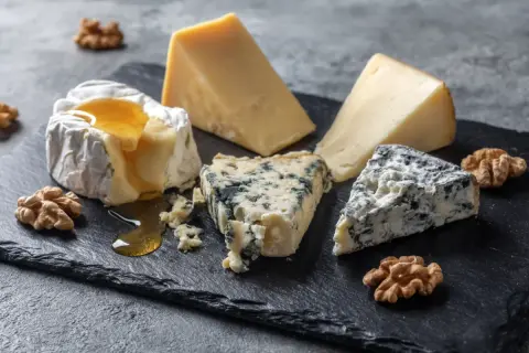 En ostbricka med brie, blåmögelost och en bit ost som påminner om ost comte, garnerad med valnötter och honung.