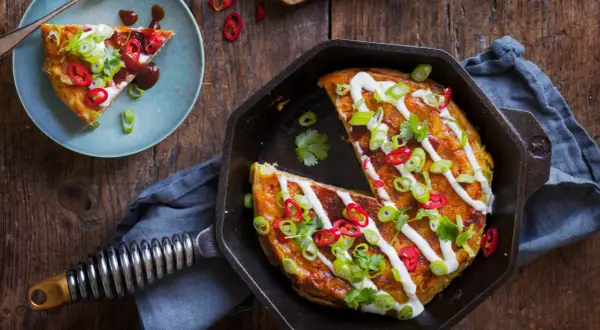 En saftig okonomiyaki i gjutjärnspanna, toppad med gräddfil, salladslök och chili. Ett perfekt recept för en smakrik middag.