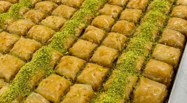 En stor bricka med gyllene, saftiga baklava-bitar, strödda med gröna pistagenötter. Perfekt för ett baklava recept.