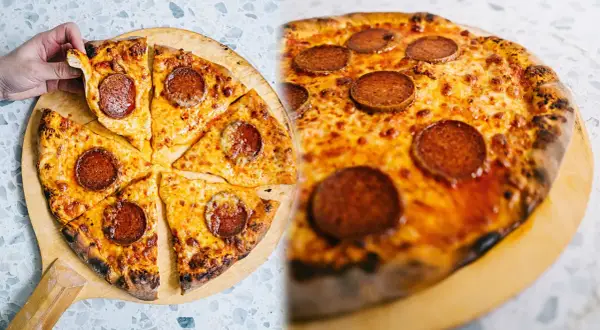 En hand tar en bit av en utsökt pepperoni pizza, perfekt för ett äkta new york pizza recept.