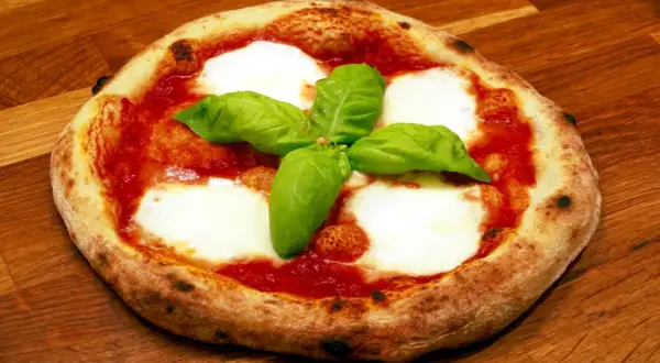 En napolitansk pizzadeg snabb, toppad med tomatsås, mozzarella och färsk basilika, ligger på en träyta.