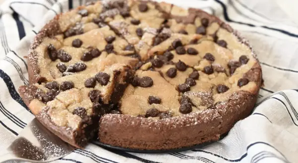 En kladdkaka med cookie dough och chokladbitar, pudrad med florsocker. En bit är uppskuren.