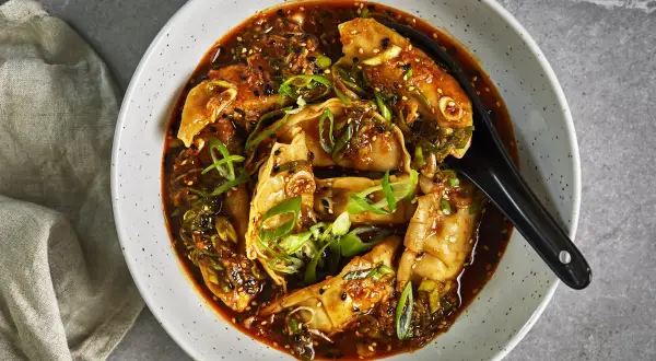 En skål med ångande dumplings i en kryddig sås, toppad med salladslök och sesamfrön. Perfekt för snabba vegetariska recept.