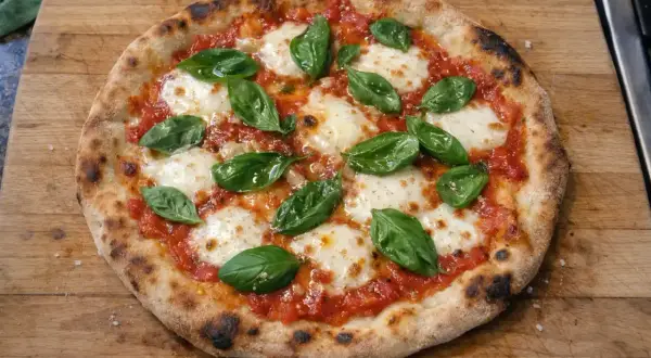 En nybakad pizza med tomatsås, smält mozzarella och färsk basilika på en träskärbräda.