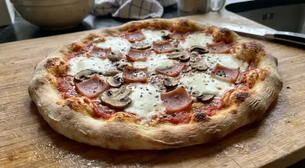 En nybakad pizza siciliana med skinka och champinjoner på en skärbräda.