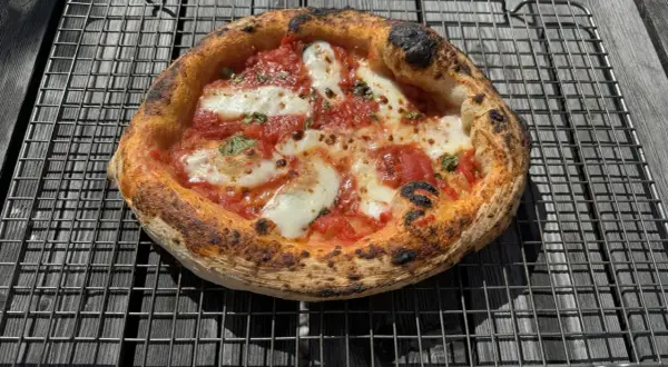 En nybakad pizza med bubblig pizzadeg 6 timmar, tomatsås och mozzarella vilar på ett galler.