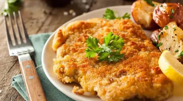 En gyllene schnitzel med dubbel panering, serverad med rostade potatisar och citronklyfta.