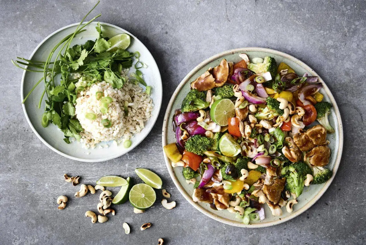 Två tallrikar med mat: en med ris, koriander och lime, den andra med kyckling, grönsaker och cashewnötter. Perfekt för enkla nyttiga recept.