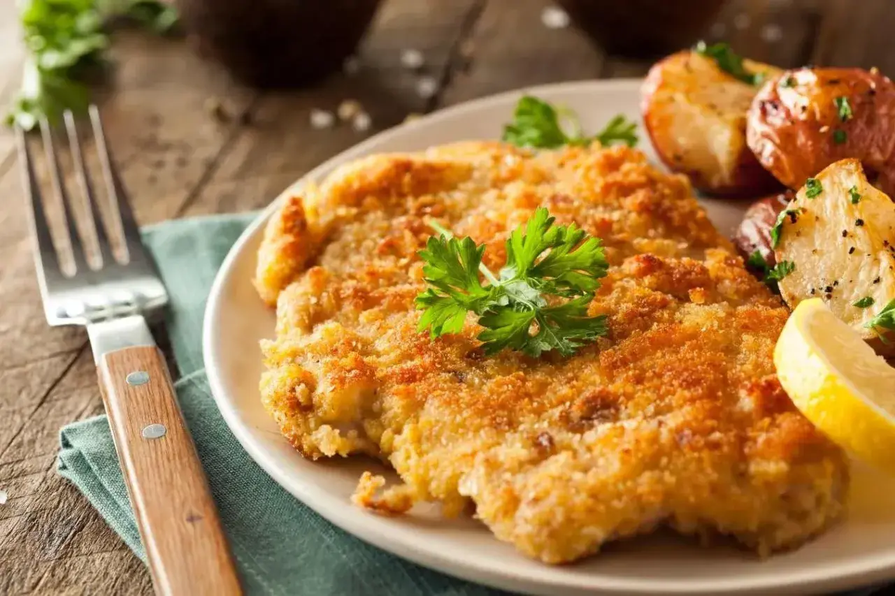 En gyllene schnitzel med dubbel panering, serverad med rostade potatisar och citronklyfta.