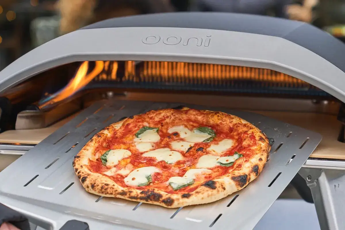 En perfekt Margherita-pizza tas ur en Ooni pizzaugn. Den gyllene ooni pizzadegen har bubblor och lite brända kanter.