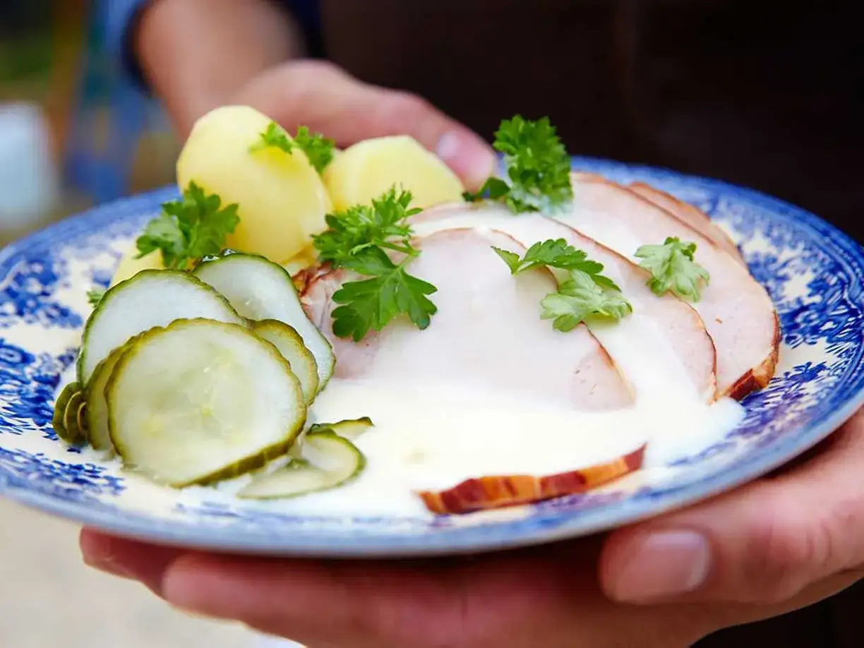 En tallrik med skivat kassler, potatis, gurka och en krämig sås. Ett klassiskt kassler recept som ser utsökt ut.